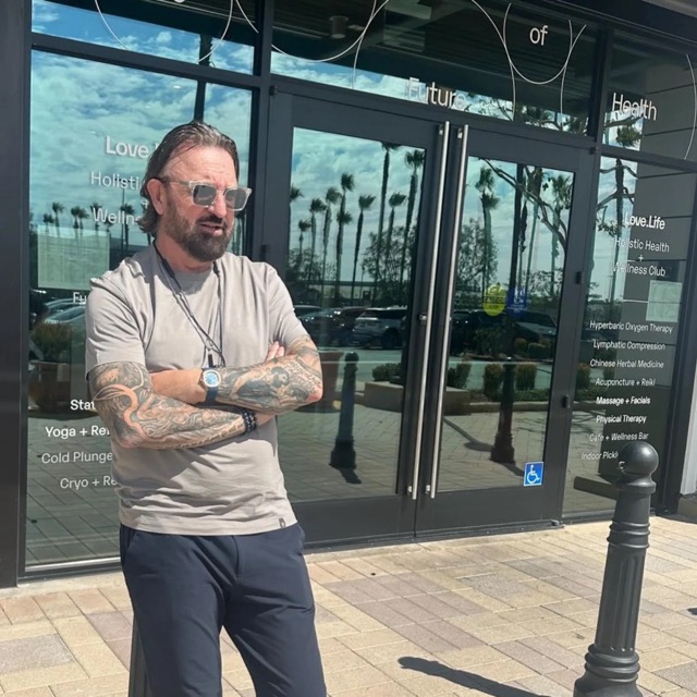 Terry Fisher in sunglasses, arms folded, outside a glass-fronted building