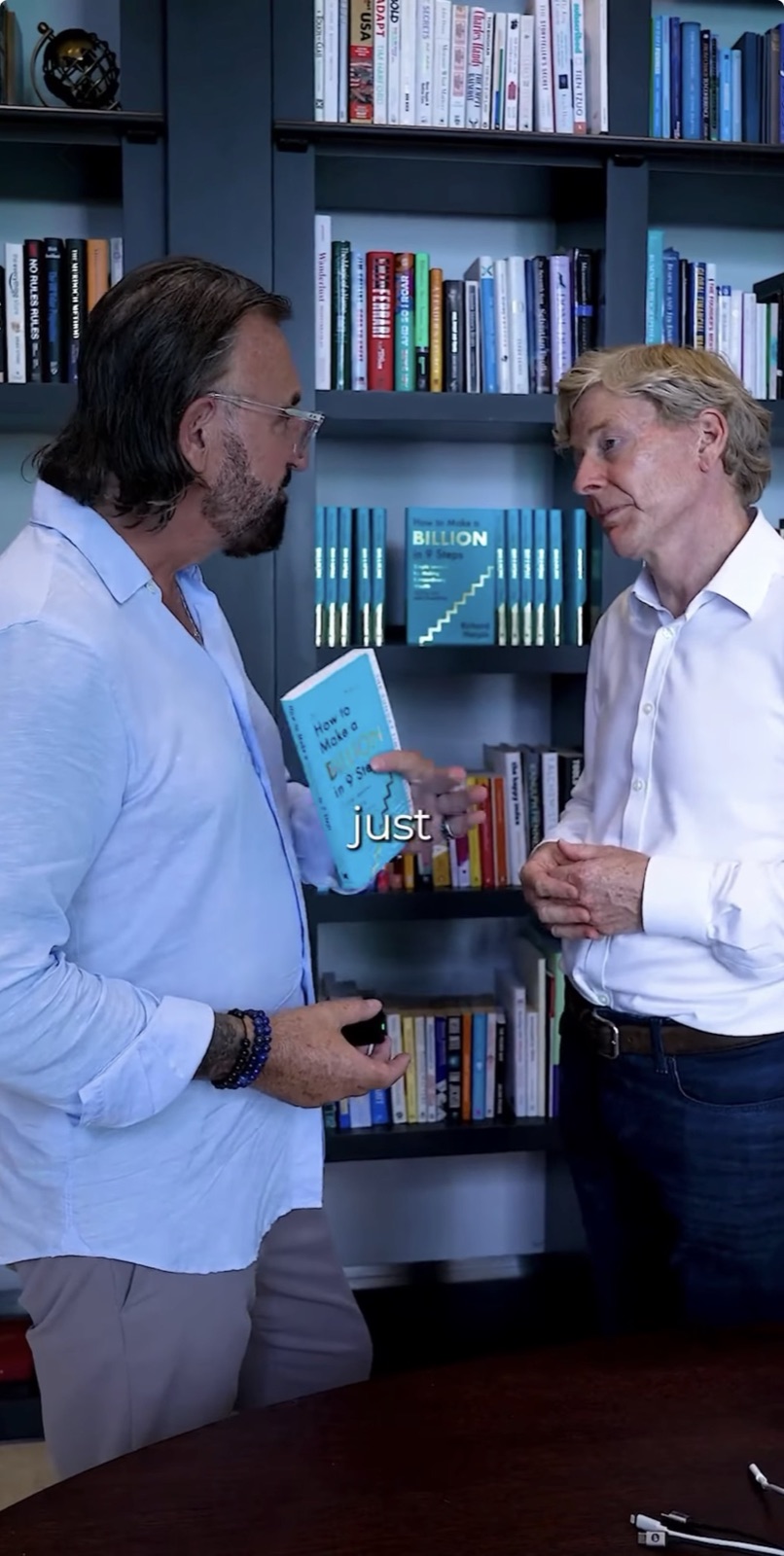 Terry Fisher holding a copy of How to Make a Billion in 9 Steps, in conversation with Sir Richard Harpin