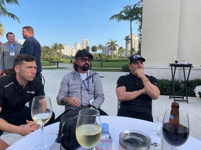 Terry Fisher at an outdoor table with Grant Cardone, a golf course and towers behind